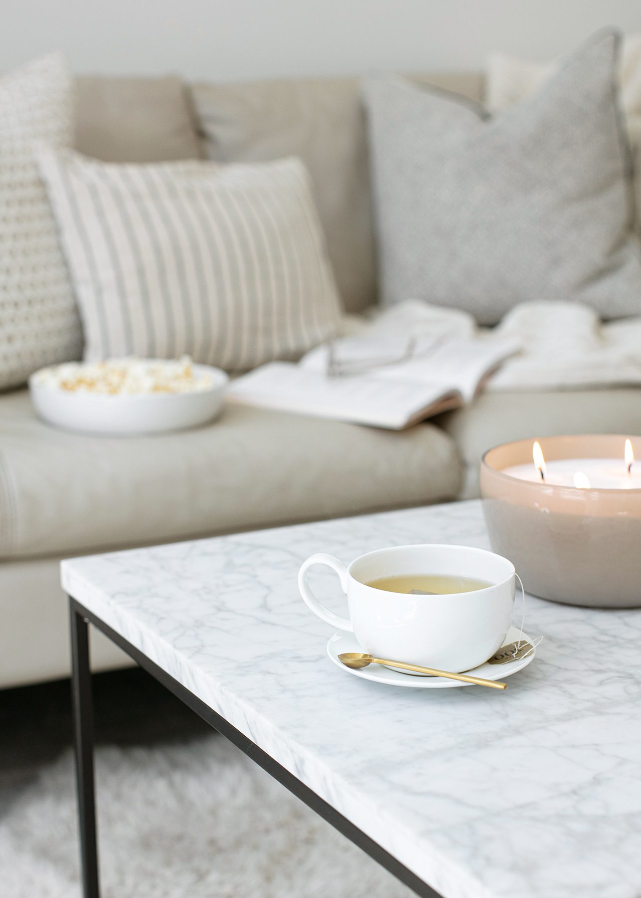 coffee table with cup of tea and candle in front of couch in living space.