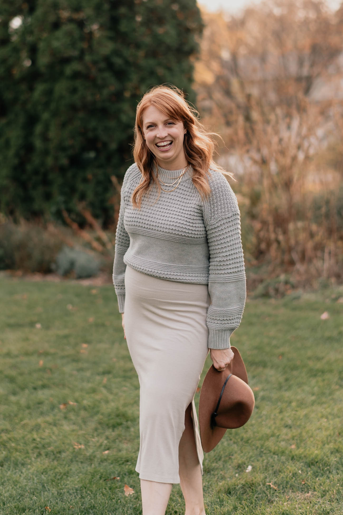 White female standing holding a hat in a sweater and skirt