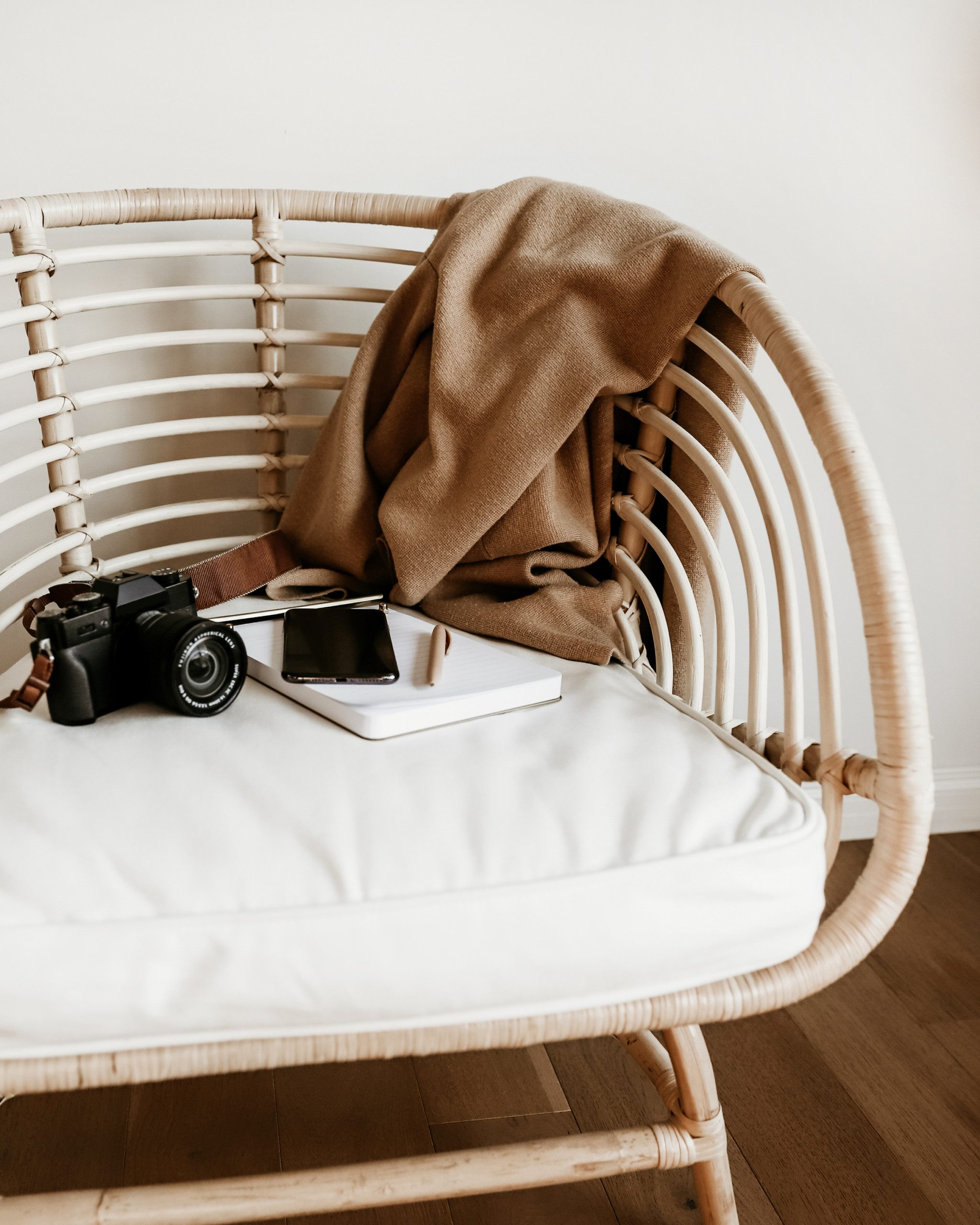 rattan chair with blanket, camera and notebook and pen sitting on top.